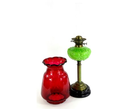 A late Victorian brass oil lamp, with associated ruby tinted shade, the green glass reservoir moulded with scrolls etc., on a