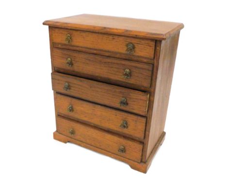 An early 20thC oak miniature chest, the top with a moulded edge above five drawers, each with brass drop handles on bracket f