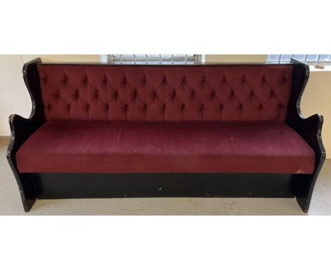 A vintage painted black wooden bench seat with button backed red velour upholstery and shaped ends. Obtained from a local pub