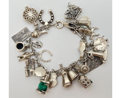 A vintage silver charm bracelet with 27 silver and white metal charms. Stamped silver on spring ring clasp. Charms include: a