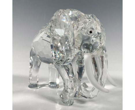 A majestic elephant stands with one foot raised, featuring black crystal eyes and frosted tusks. Swarovski backstamp. This it