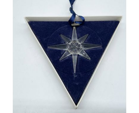 A clear, faceted eight-point snowflake ornament, hanging from a satin navy-blue satin ribbon, with a metal tag impressed with