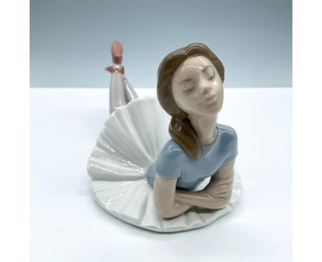 Glossy figure of a ballerina laying on the ground with her arms crossed. Lladro backstamp. This item has its original box, di