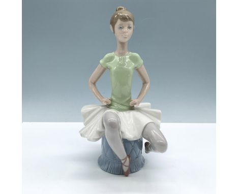 Glossy porcelain figure of a young lady in ballet shoes and skirt, sitting on a tufted stool. Lladro backstamp. This item has