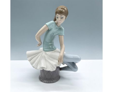 Glossy porcelain figure of a ballet dancer sitting on an ottoman wearing a blue blouse and white skirt. Lladro backstamp. Inc