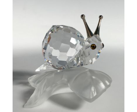 A charming snail rests on a frosted vine leaf, featuring blue crystal eyes and rhodium antennas. Swarovski backstamp. This it