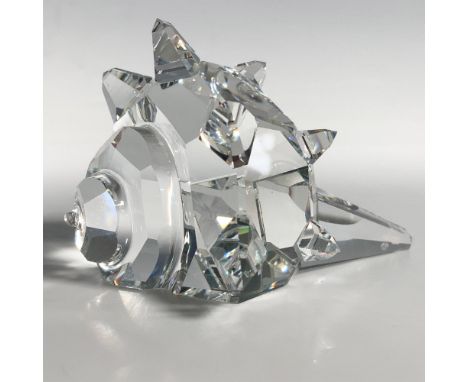 A conch shell showcases a spiral body and long point, adorned with numerous spikes around the tip. Swarovski backstamp. This 