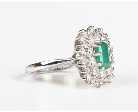 An 18ct white gold, emerald and diamond cluster ring, claw set with a cut cornered rectangular step cut emerald within a two 