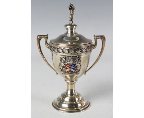 A George VI silver golf trophy cup and cover with golfer finial, the urn shaped body with enamelled armorial flanked by a pai