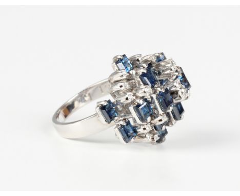 A white gold, sapphire and diamond cluster ring in a raised abstract design, mounted with square cut sapphires and circular c