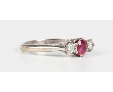 An 18ct white gold, ruby and diamond three stone ring, claw set with the oval cut ruby between two circular cut diamonds, Lon