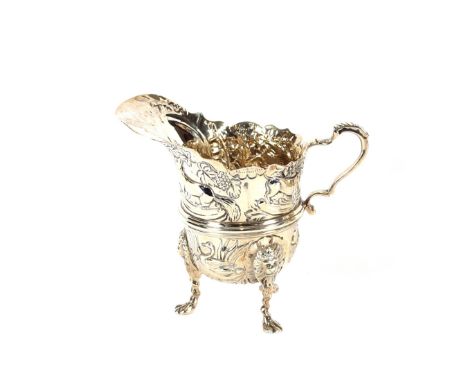 An Edwardian Irish silver cream jug, of helmet shape, profusely embossed with birds, animals and flowers, raised on three lio