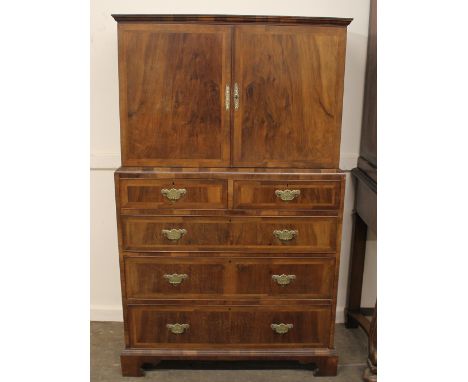 An 18th Century style walnut and cross-banded cupboard on chest, the upper shelves enclosed by a pair of cross-banded doors, 