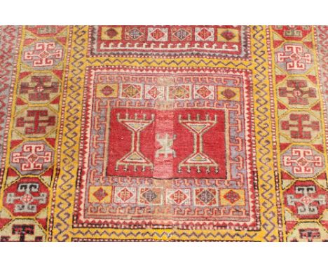 an Eastern rug, decorated with three central panels with stylised emblems, with geometric border surround, on red ochre and g
