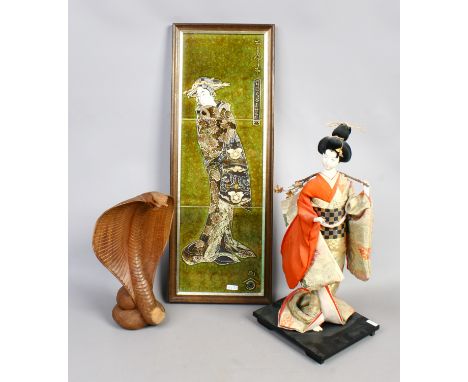 Three Eastern decorative items including a Japanese doll on stand, a Chinese tile display and a carved wood model of a cobra.