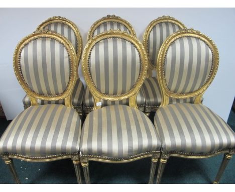 A SET OF SIX CONTINENTAL GILTWOOD AND UPHOLSTERED CHAIRS each with a flowerhead cresting above an oval upholstered panel and 