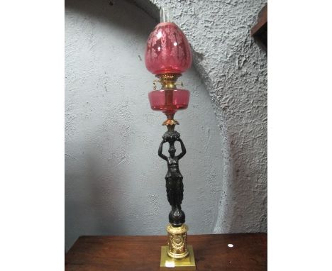 A FINE GILT BRASS FIGURAL OIL LAMP with ruby etched glass shade and reservoir raised the cylindrical base moulded in relief w