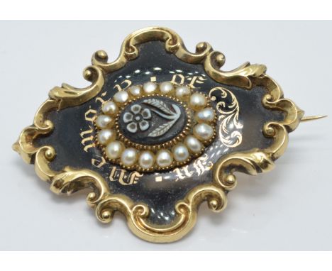 A Victorian enamel mourning brooch set with a flower plaque, black enamel and seed pearls reading 'In Memory of' verso a glas