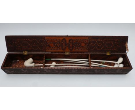 A 19thC pokerwork decorated clay pipe box with long clay pipes within, the box W66 x D9.5 x H10cm, the longest pipe 44cm