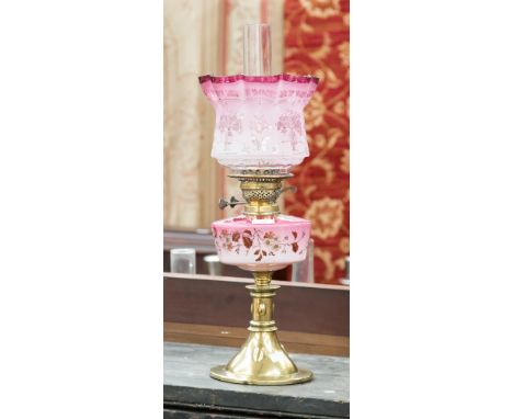 A late Victorian brass oil lamp with ruby opaque glass reservoir/shade