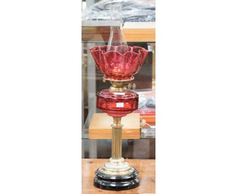 A late Victorian brass oil lamp with ruby glass reservoir/shade