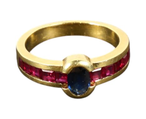 An 18ct gold ring set with a central sapphire flanked by ruby set shoulders, size M