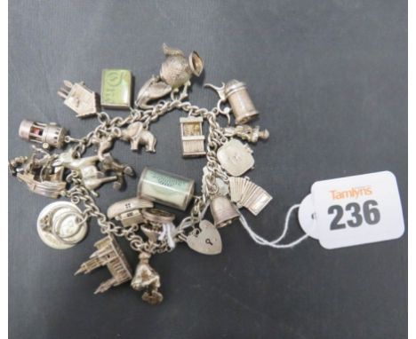 A silver charm bracelet with padlock clasp, attached charms include an accordion, a stein, a church, a donkey, emergency £1 n