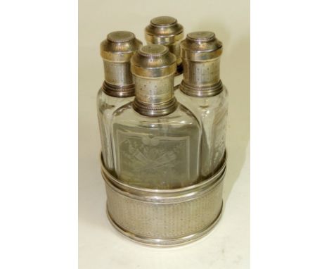 A late 19th Century French silver circular stand containing a set of four shaped clear glass scent bottles each having silver