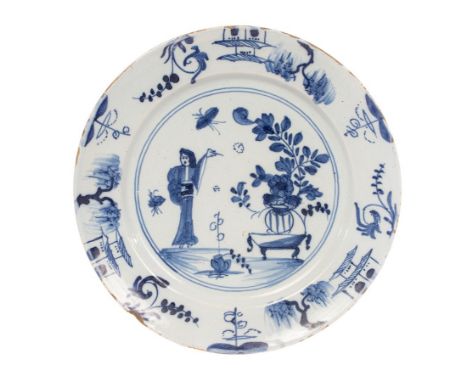 An English Delftware plate, circa 1740-50, painted in blue with a Long Eliza figure and a potted plant on a low table, the bo