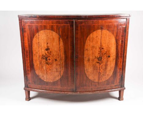 A George III satinwood crossbanded mahogany bowfront two-door drawing room cabinet, the shaped doors each with an inlaid oval