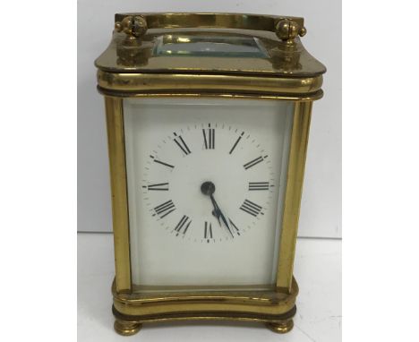 An early 20th Century lacquered brass cased carriage clock of waisted rectangular form raised on turned feet, the enamelled d