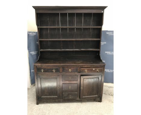 An 18th Century Welsh oak dresser, the boarded three tier plate rack with moulded cornice over four central drawers flanked b