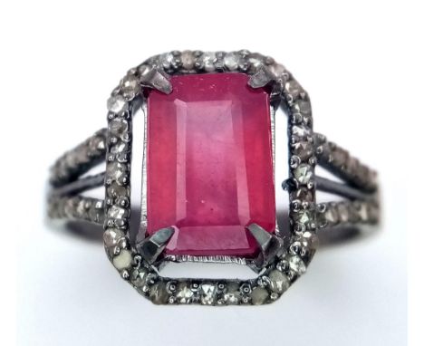 A Rectangular Shaped Ruby and Diamond Ring set in 925 gun-metal silver. Central ruby with diamond surround. Size N. Ruby- 3.7