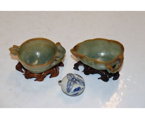 Two carved jade coloured hardstone libation cups on hardwood stands and a blue and white water dropper