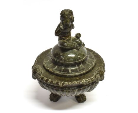 A CARVED SERPENTINE LIDDED BOWL  the finial modelled as a cherub, the bowl with three masks and paw feet, 19cm high overall