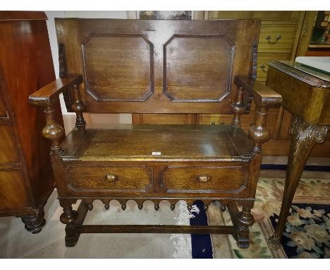 An oak Jacobean style monk’s bench heavily carved, with panelling, on bulbous column supports