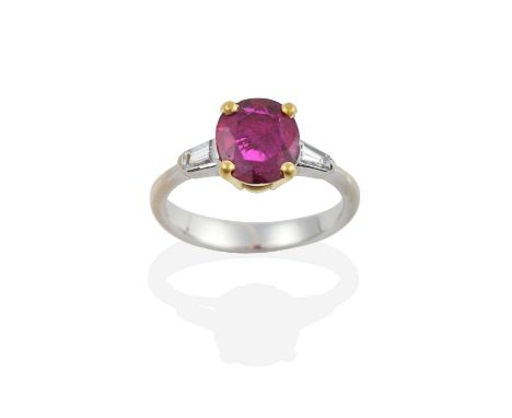 A Ruby and Diamond Ring, the oval cut ruby in a yellow four claw setting, flanked by tapered baguette cut diamonds in white c