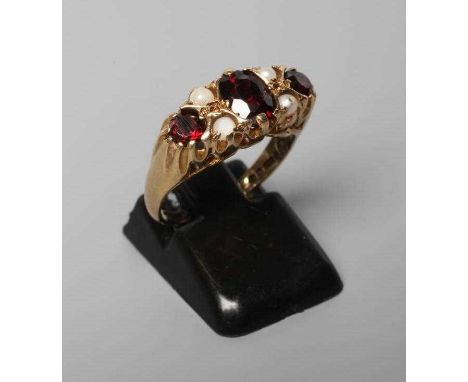 A THREE STONE GARNET RING, the facet cut stones claw set with four seed pearls between, on carved shoulders and a plain 9ct g
