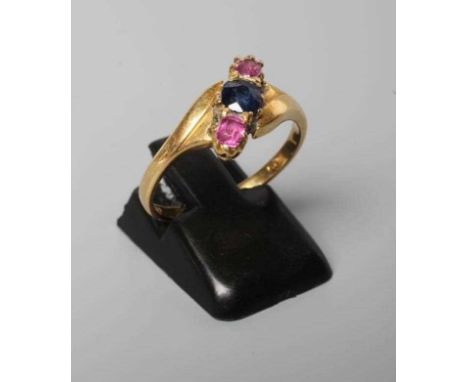 A SAPPHIRE AND GARNET THREE STONE CROSSOVER RING, the central circular facet cut sapphire flanked by two smaller garnets, all