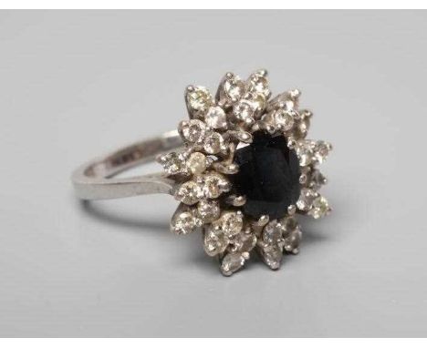 A SAPPHIRE AND DIAMOND CLUSTER RING, the oval facet cut sapphire claw set to a border of sixteen pairs of small brilliant cut