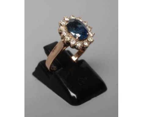 A SAPPHIRE AND DIAMOND CLUSTER RING, the oval facet cut sapphire claw set to a border of fourteen small brilliant cut diamond