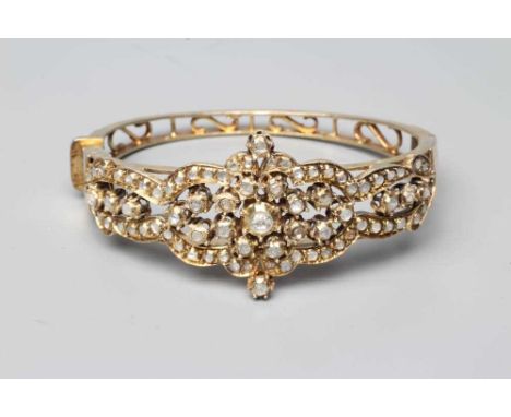A DIAMOND STIFF HINGED BANGLE, the open upper section set with numerous mix cut stones in rub-over settings to a plain unmark