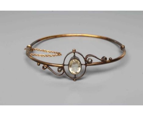 A VICTORIAN STIFF HINGED BANGLE, the upper section centred by an open back collet set oval facet cut citrine, between open sc