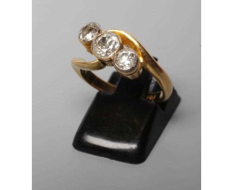 A THREE STONE DIAMOND CROSSOVER RING, the mix cut stones totalling approximately 1ct, collet set to a plain shank stamped 18,