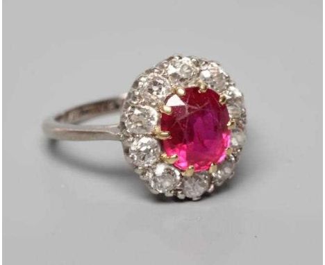 A RUBY AND DIAMOND CLUSTER RING, the oval facet cut ruby claw set to a border of ten brilliant cut diamonds each of aproximat