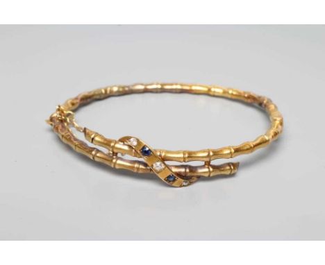 A LATE VICTORIAN STIFF HINGED FAUX BAMBOO BANGLE, the open and over lapping upper section tied by an oblong panel gypsy set w