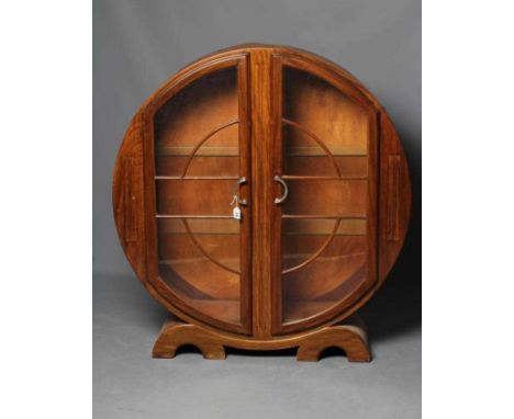 AN ART DECO WALNUT DISPLAY CABINET of circular outline with two astragal glazed doors enclosing glass shelving, stepped chrom