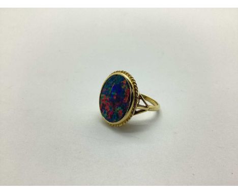 An 18ct Gold Black Opal Doublet Single Stone Panel Ring, oval collet set, within ropetwist setting, between trifurcated shoul