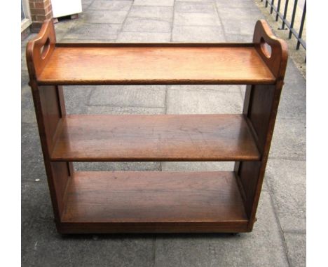 AN OAK THREE-TIER ARTS & CRAFTS BOOKSTAND ,the panelled sides with pierced handles, on ceramic casters, 95cm wide, 38cm deep,