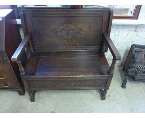 A stained oak monks bench with fold over top above a hinged top seat over blind fretwork raised on turned baluster supports j